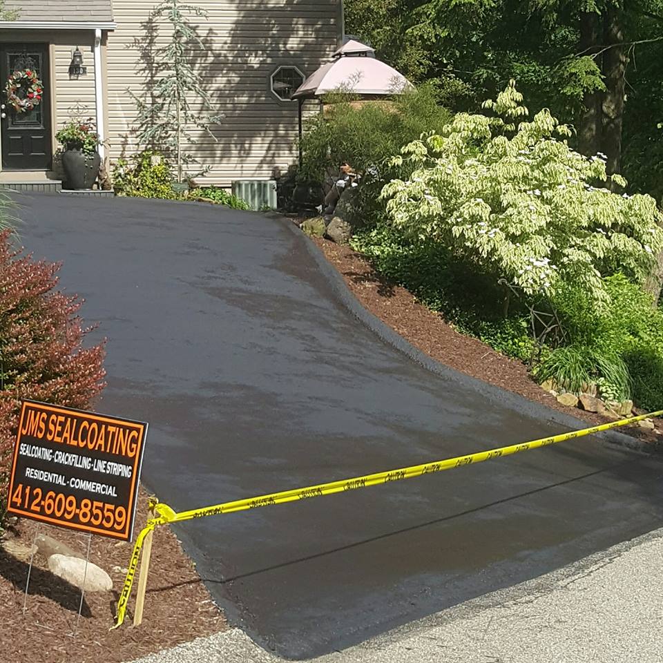 Freshly sealcoated residential driveway with a JMS Sealcoating job sign